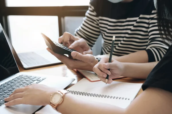 Manually calculating expenses with a laptop and a calculator.